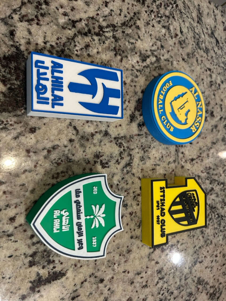 Colorful 3D printed football club logos on a granite surface, showcasing unique designs.