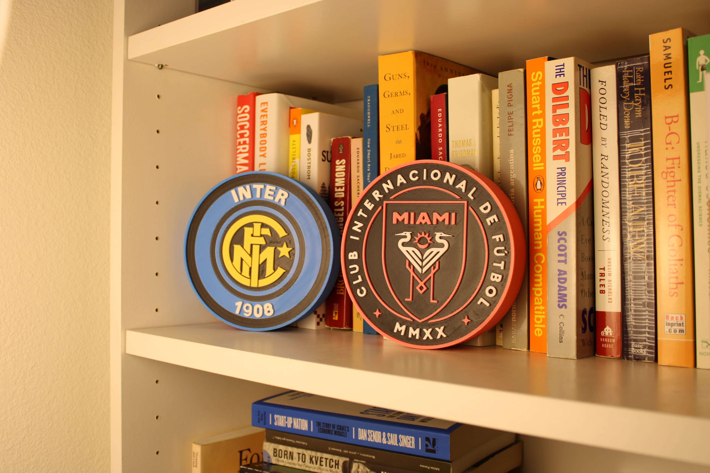 Stylish Inter Miami and Inter Milan 3D Printed Emblems on a bookshelf, perfect decor for soccer fans.