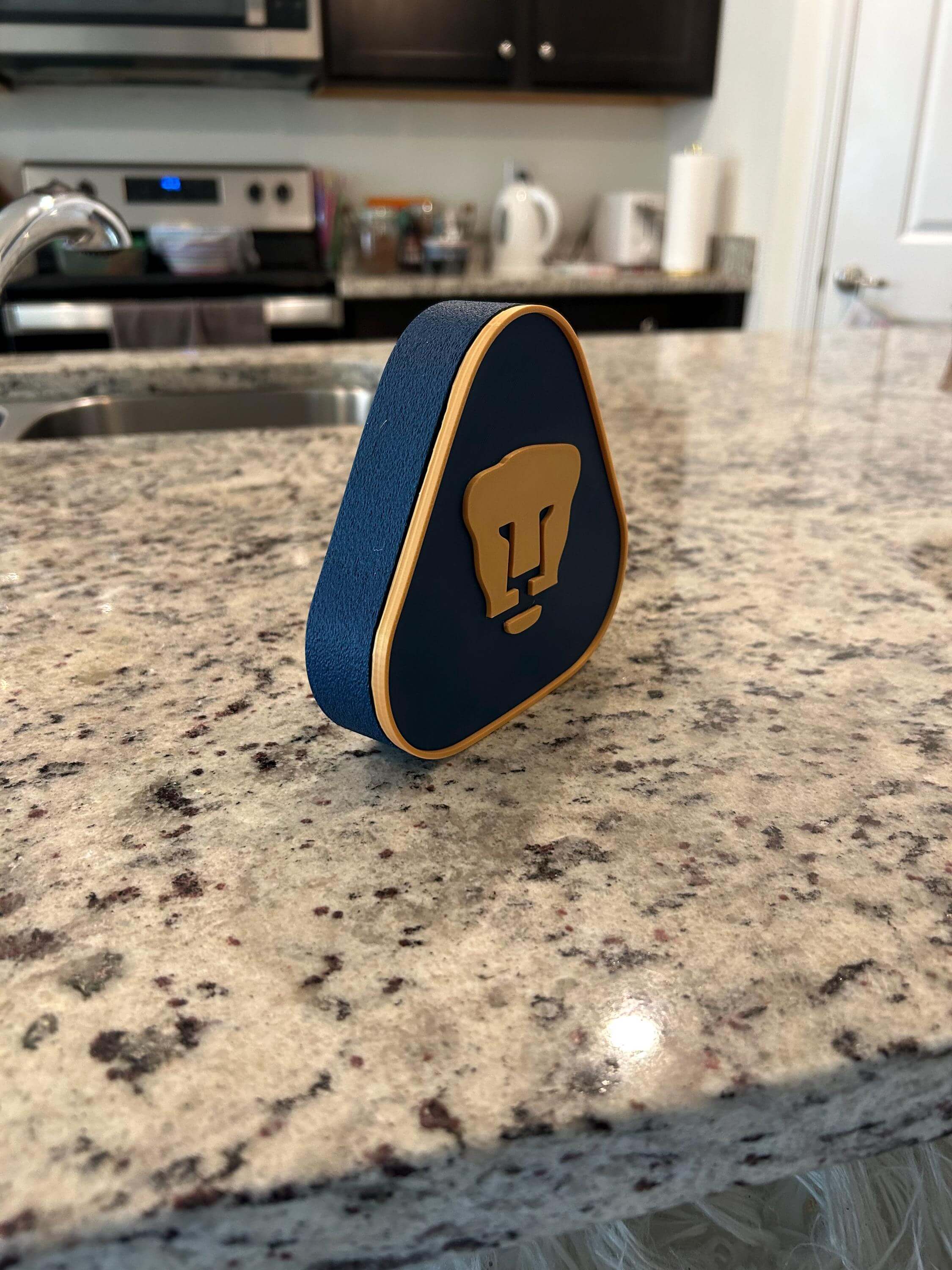 3D printed Pumas UNAM plaque on a kitchen countertop, featuring vibrant colors and unique design for soccer fans.