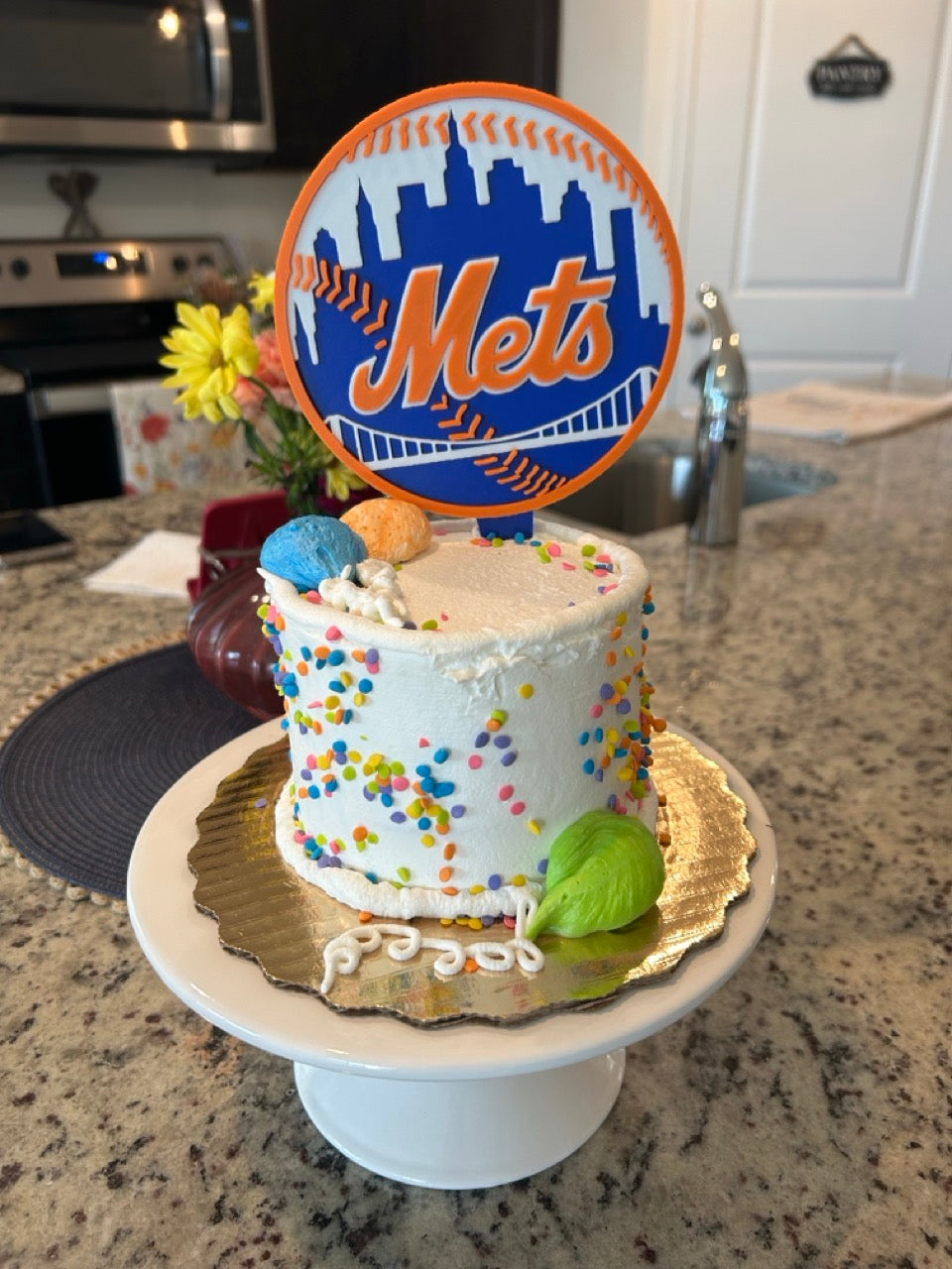 Mets cake topper inserted in a real white sprinkle birthday cake on a kitchen counter — front view