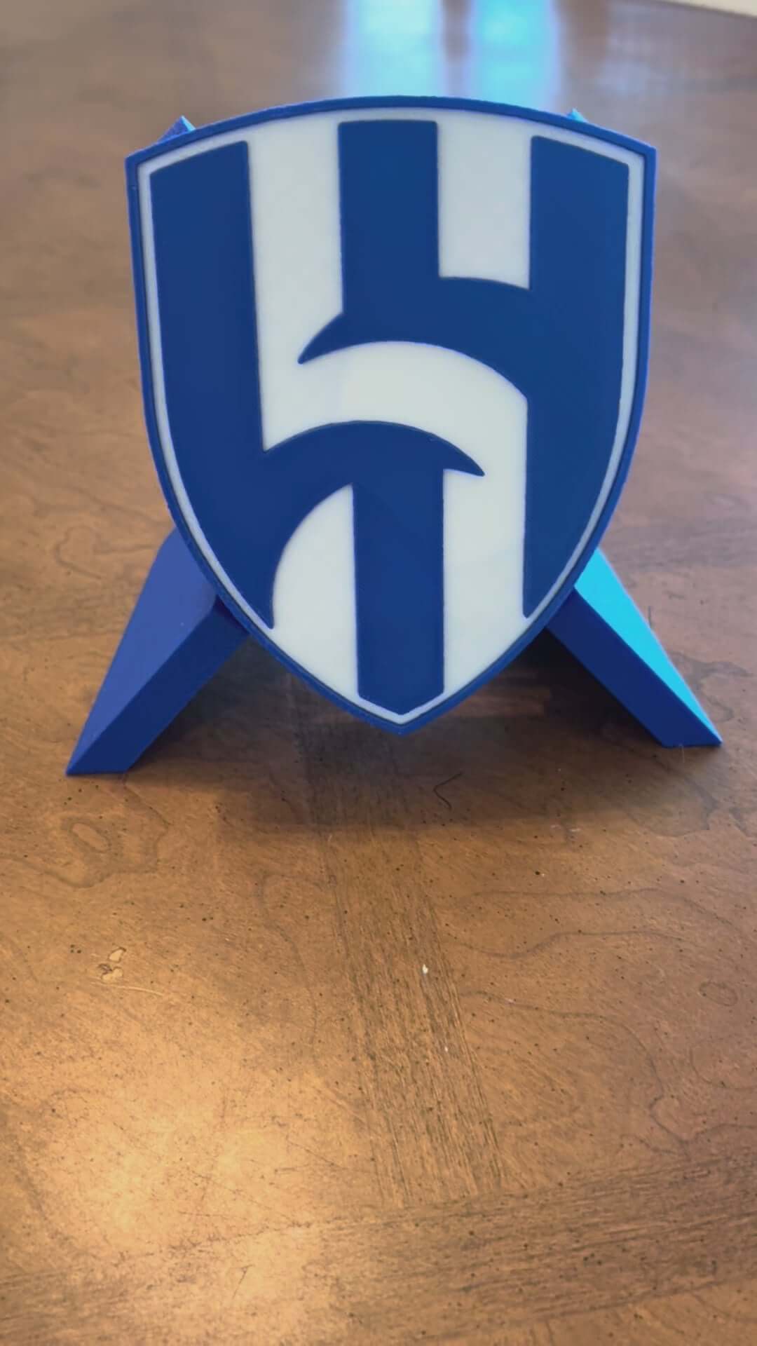 Load video: Custom Al Hilal FC 3D printed plaque stands on a wooden surface, showcasing vibrant blue colors and a detailed crest design.